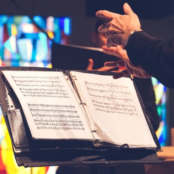 A conductor’s hands above sheet music sitting on a music stand