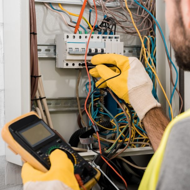 cropped image of electrician checking electrical box with multimetr in corridor