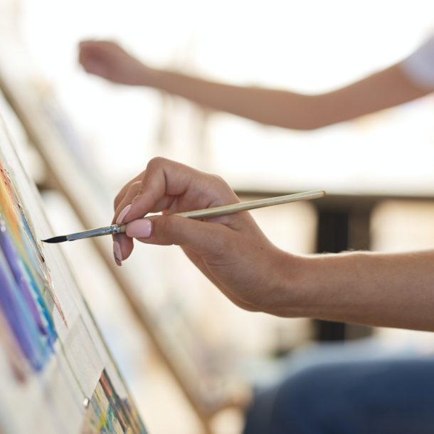 Girls hand holds a paint brush. Process of painting picture at the easels in the art studio