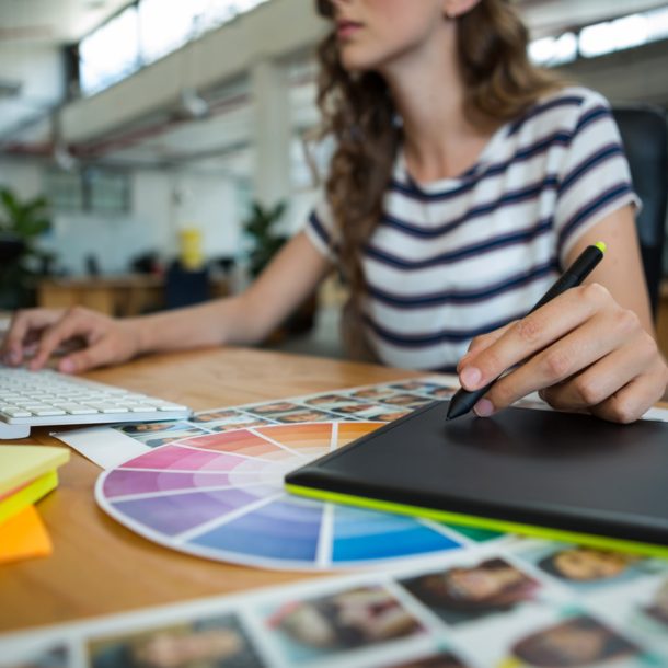 Mid section of female graphic designer using graphics tablet at desk