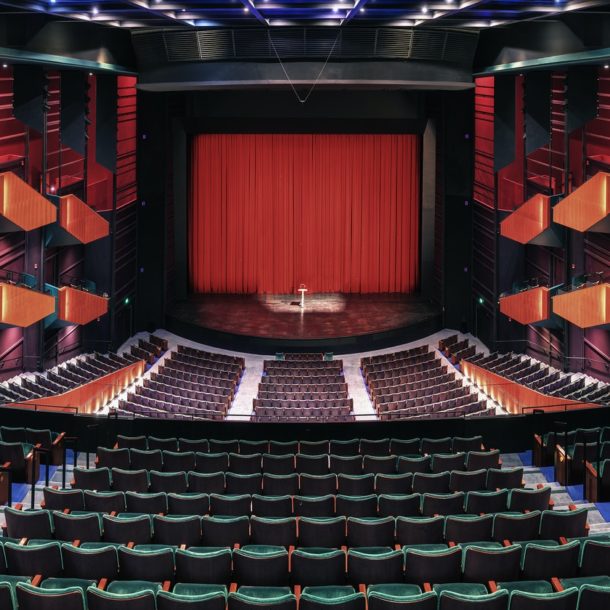 Empty theatre auditorium, stage with a red curtain, boxes and modern design.