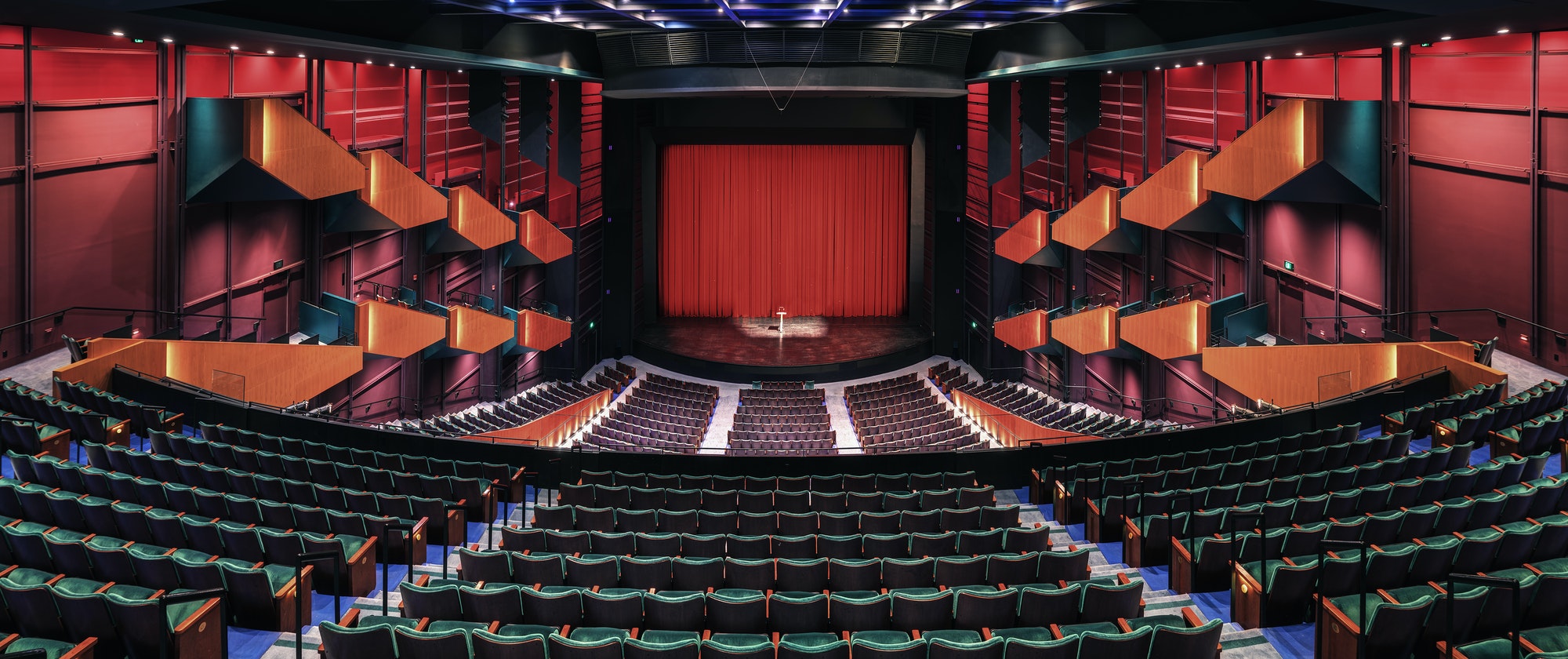 Empty theatre auditorium, stage with a red curtain, boxes and modern design.