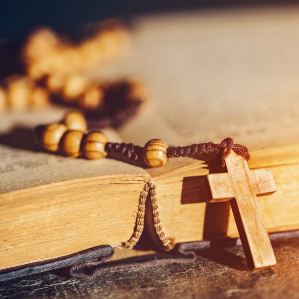 Rosary with cross laying on a Bible book.