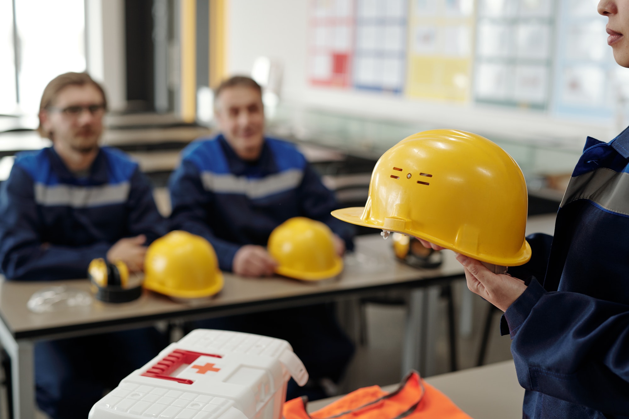 Young female worker in uniform holding protective helmet while standing in front of male colleagues