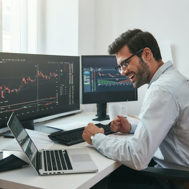 Lucky day. Happy young businessman or trader in formalwear and eyeglasses using laptop and smiling